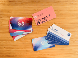 Two different business cards sit on a wood table. One is more simple on front and has four back design variations. The other is more detailed and only has one design variation on the rear.