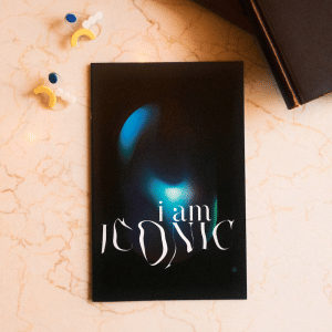 'I am ICONIC' zine cover, a dark but colorful art piece inside an elongated capsule shape with the text 'i am' in a fine serif white font and the text 'ICONIC' in capital white warped letters.